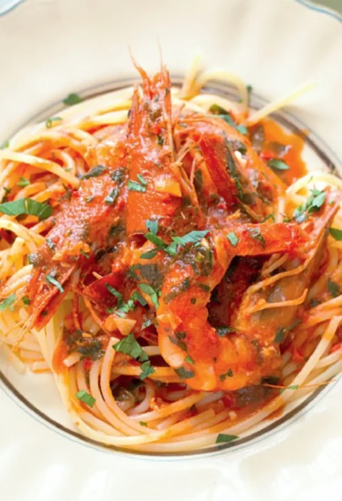 Spaghetti for Pinuccia with whole jumbo shrimp in tomato sauce and chopped herbs in a white bowl