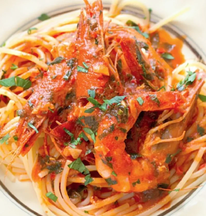 Spaghetti for Pinuccia with whole jumbo shrimp in tomato sauce and chopped herbs in a white bowl