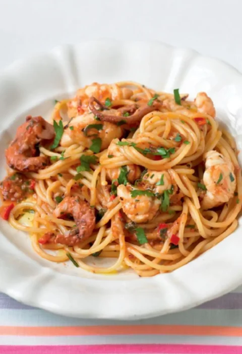 Spaghetti in the Square on a white plate with seafood pieces in a tomato sauce and chopped parsley