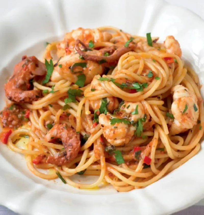 Spaghetti in the Square on a white plate with seafood pieces in a tomato sauce and chopped parsley