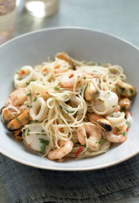 Spaghettini with seafood sauce with shrimp, squid rings, mussels and scallops in a shallow gray bowl
