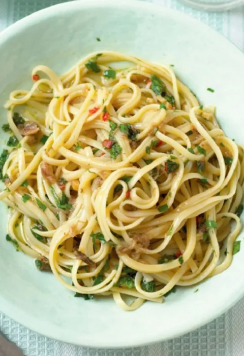 A pale green bowl of sparrow tongues with anchovies, flat pasta tossed with chopped parsley and red chili
