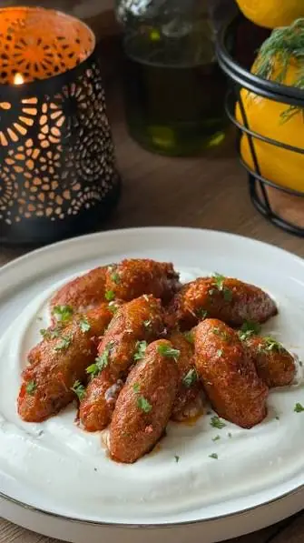 Spiced bulgur meatballs topped with parsley on a plate of garlic yogurt