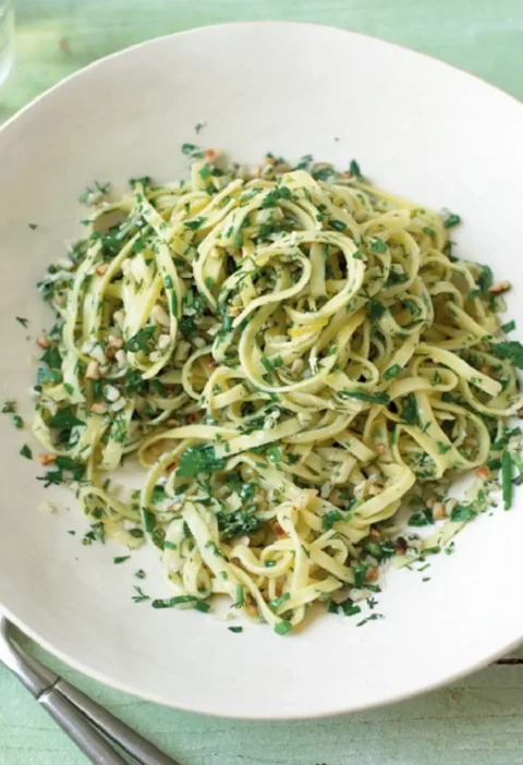 Springtime tagliolini with chopped fresh herbs and hazelnuts in a white bowl on a green wooden table