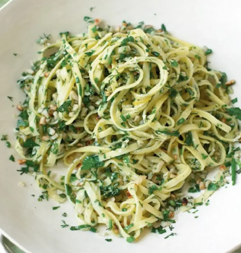 Springtime tagliolini with chopped fresh herbs and hazelnuts in a white bowl on a green wooden table