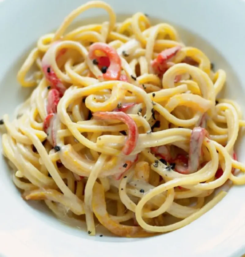 Square spaghetti with garlic and anchovy sauce and red and yellow pepper slices in a white bowl