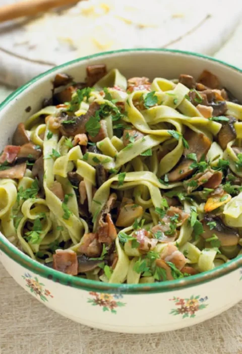 Tagliatelle verdi with field mushrooms, speck and chopped parsley in a green-rimmed floral bowl