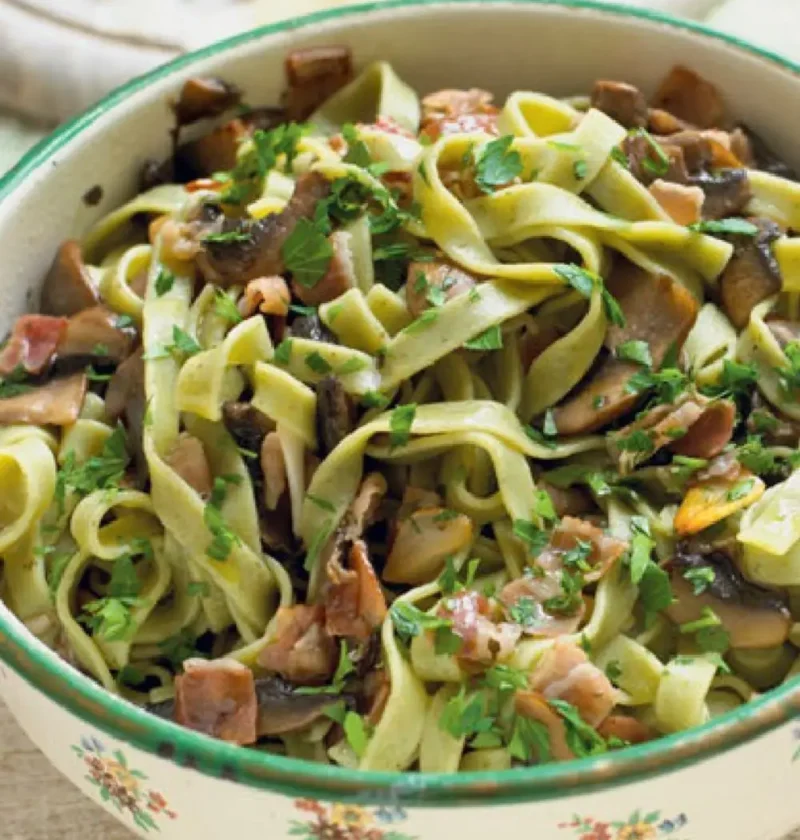 Tagliatelle verdi with field mushrooms, speck and chopped parsley in a green-rimmed floral bowl