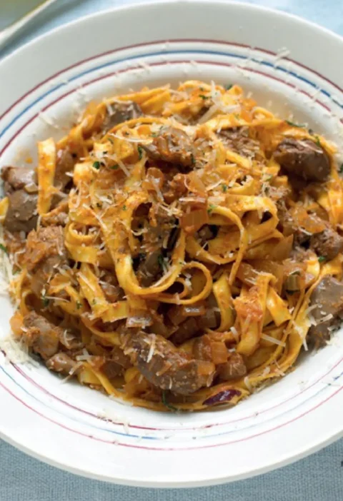 Tagliatelle with chicken livers in a white bowl with a red and blue rim, topped with grated pecorino