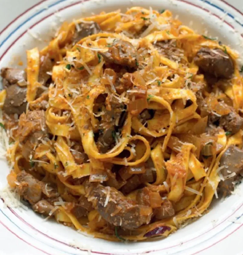 Tagliatelle with chicken livers in a white bowl with a red and blue rim, topped with grated pecorino