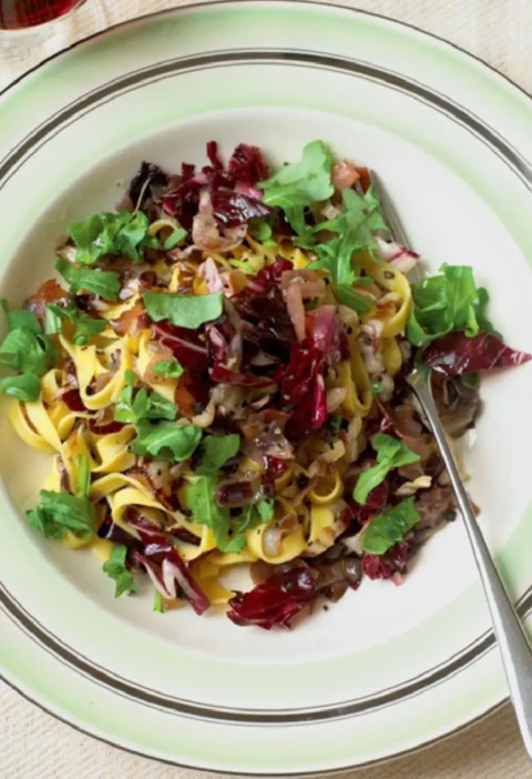 Tagliatelle with radicchio and arugula on a green-rimmed plate with red wine in the background