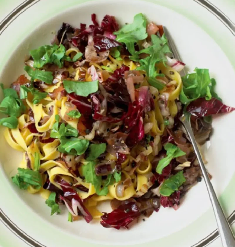 Tagliatelle with radicchio and arugula on a green-rimmed plate with red wine in the background