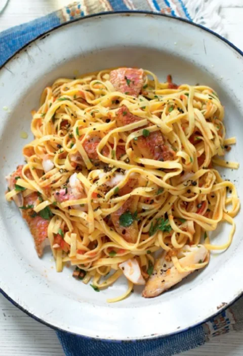 Tagliolini with red mullet fillets, tomato and chopped parsley in a white enamel bowl