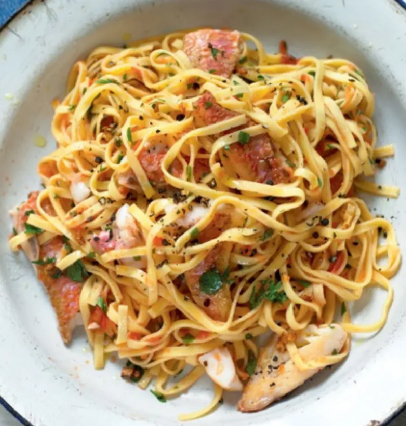 Tagliolini with red mullet fillets, tomato and chopped parsley in a white enamel bowl
