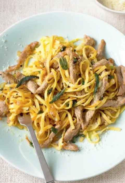 Tagliolini with veal strips and sage leaves on a pale plate with a fork and grated Parmesan nearby