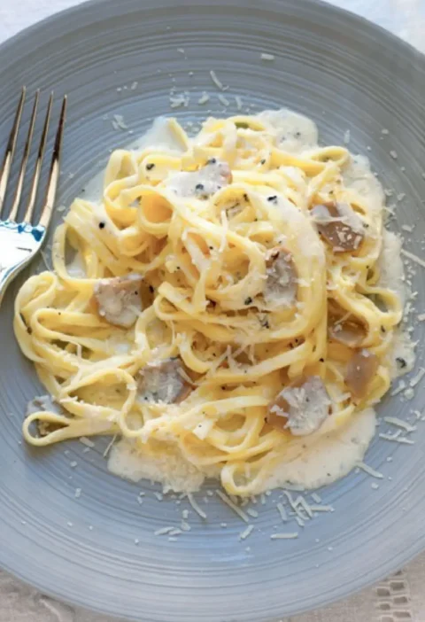 Tajarin with butter and truffle on a gray plate, with creamy sauce, grated Parmesan and truffle slices
