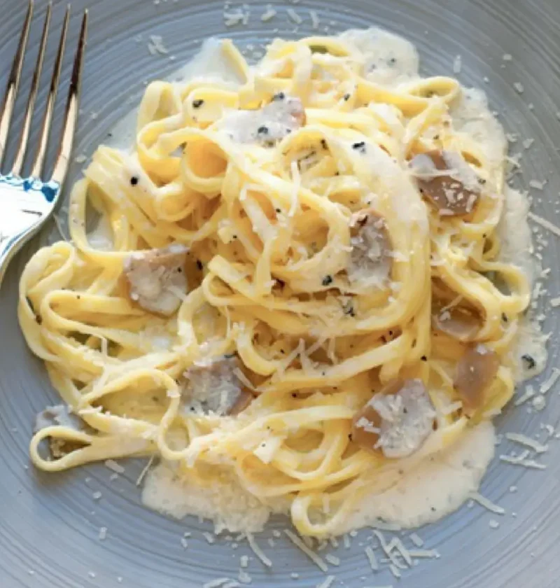 Tajarin with butter and truffle on a gray plate, with creamy sauce, grated Parmesan and truffle slices