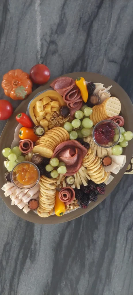 Thanksgiving charcuterie board with salami roses, crackers, grapes, blackberries and two jams on an oval platter