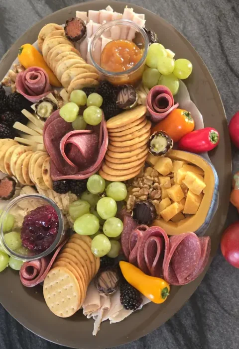 Thanksgiving charcuterie board with salami, turkey, cheddar cubes, grapes and crackers beside a small pumpkin and red apples