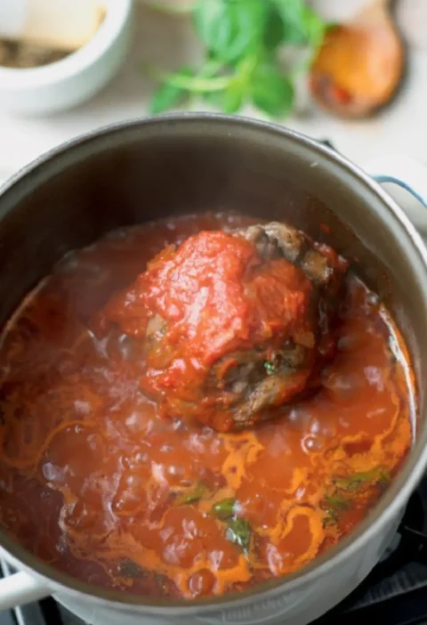 Tomato and meat ragout simmering in a pot with a bone-in piece of meat in the red sauce