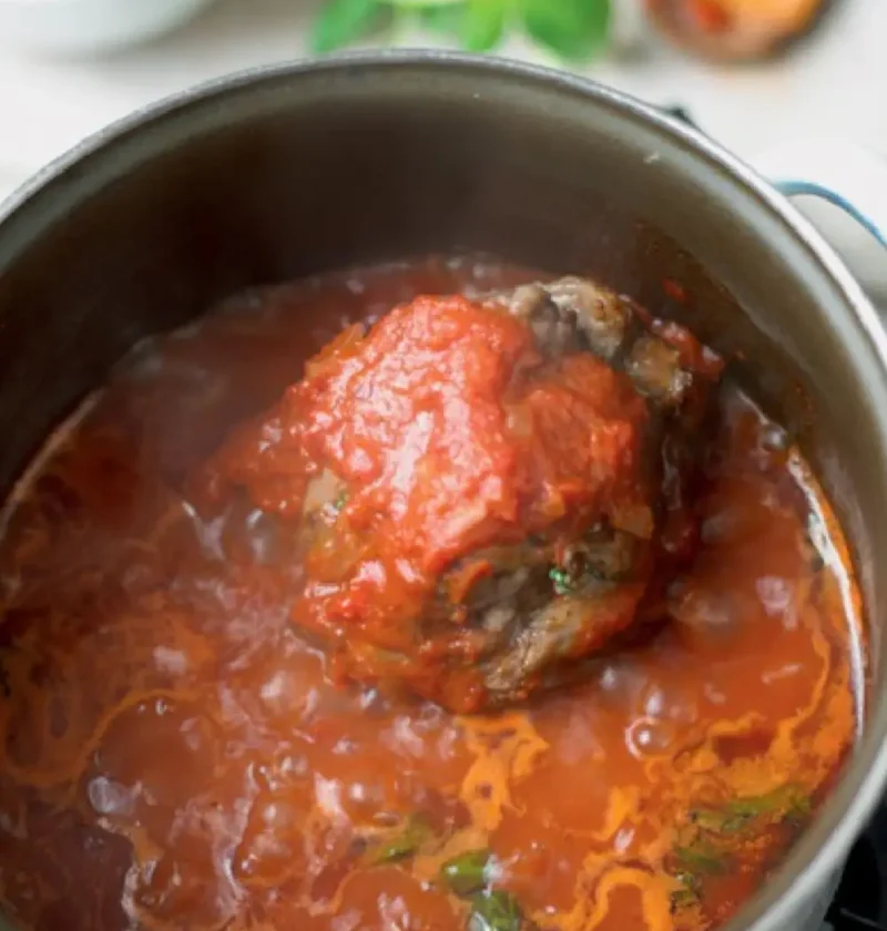 Tomato and meat ragout simmering in a pot with a bone-in piece of meat in the red sauce