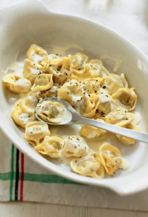 Tortellini with cream and black pepper in a white baking dish with a spoon