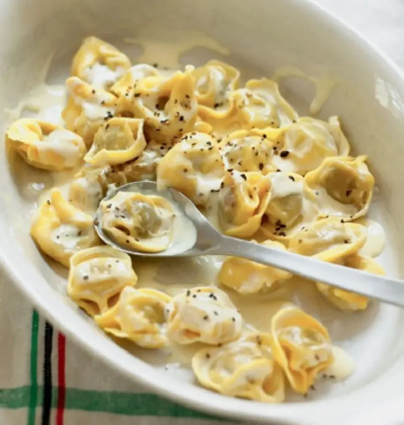 Tortellini with cream and black pepper in a white baking dish with a spoon