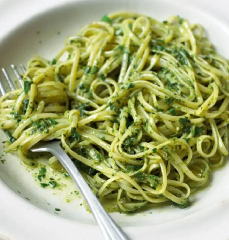 Trenette with basil sauce on a white plate with a fork, coated in bright green pesto