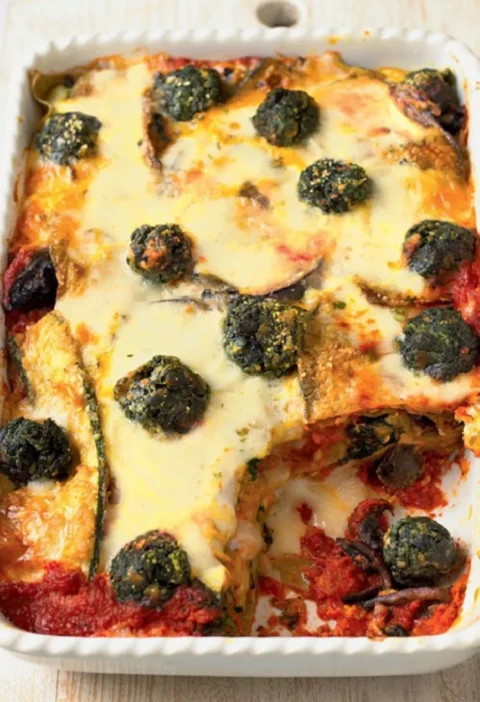 Baked vegetarian lasagne with melted cheese, spinach balls and eggplant in a white baking dish