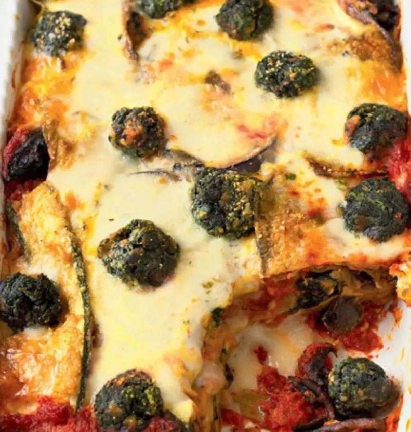 Baked vegetarian lasagne with melted cheese, spinach balls and eggplant in a white baking dish