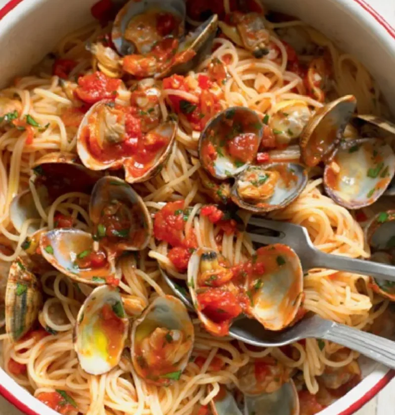 Bowl of vermicelli with clam sauce, open clam shells and chopped tomatoes with a red rim